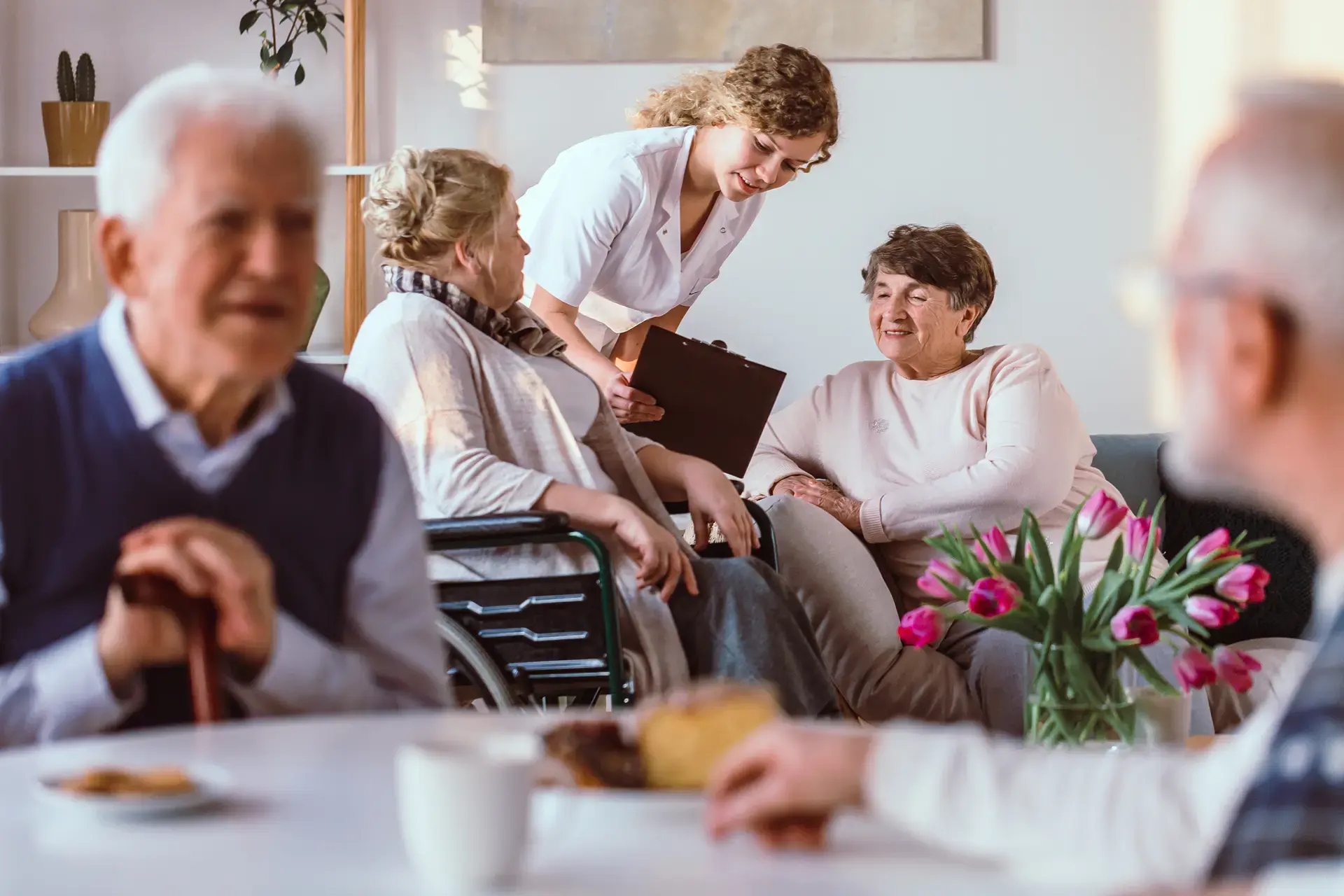 Opiekunki rozmawiają z seniorami we wspólnej świetlicy z tulipanami w Domu Seniora Kalina