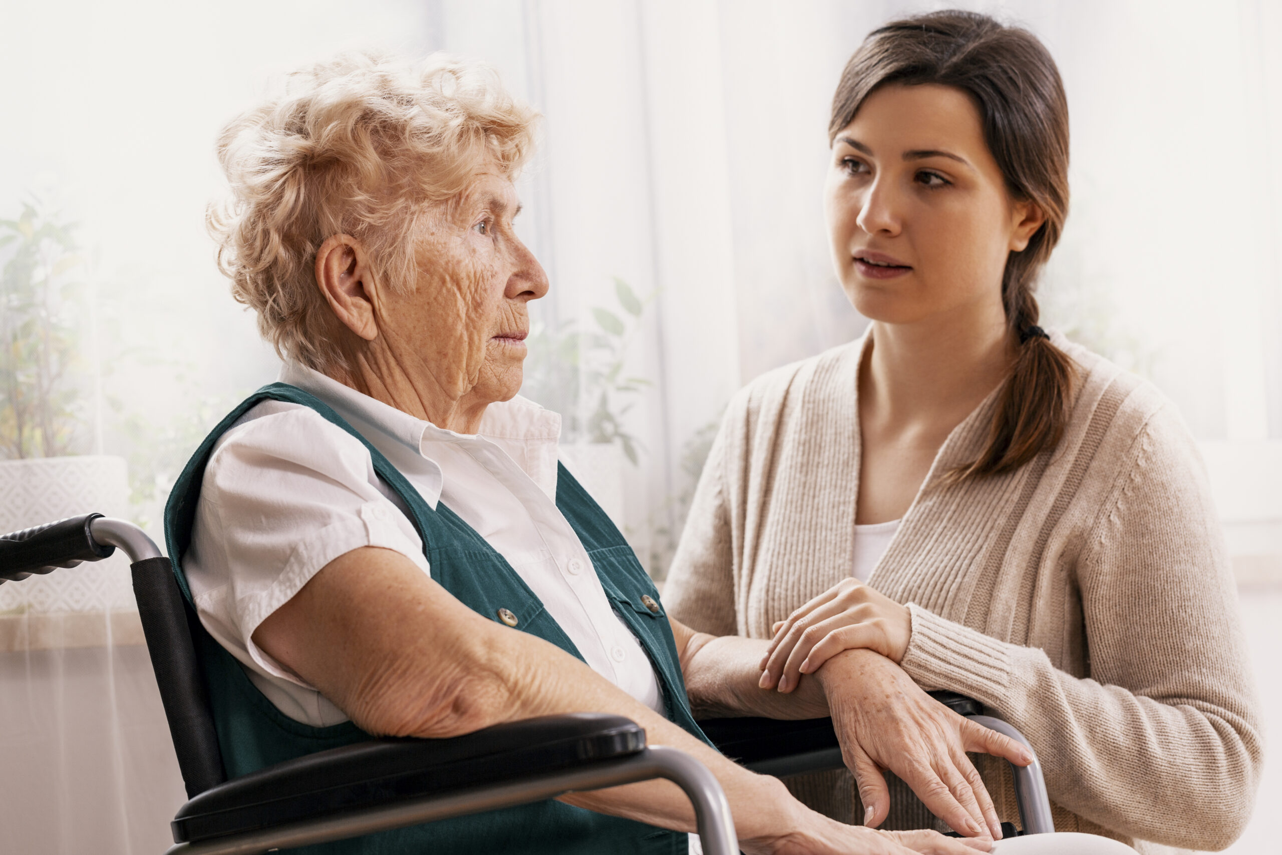 Opiekunka trzyma za rękę seniorkę na wózku inwalidzkim w prywatnym domu opieki w Gdańsku